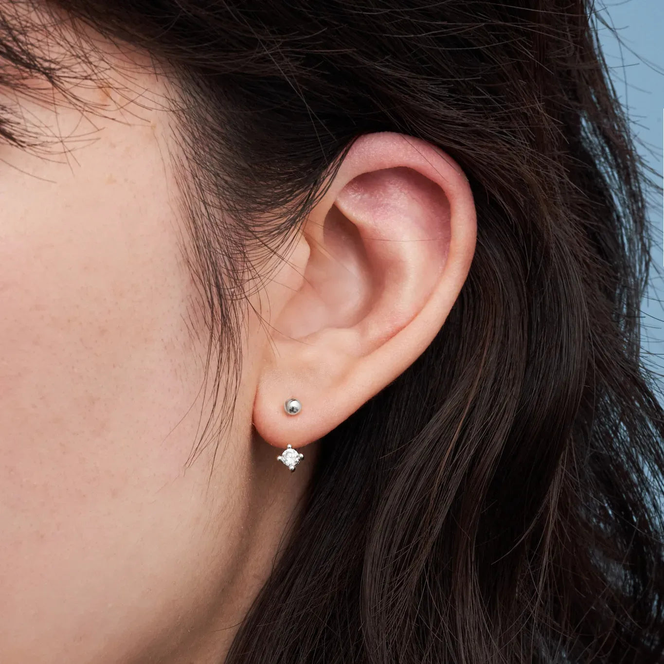 Close-up of an ear wearing a silver earring with a dark background