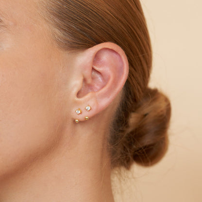 Close-up of an ear wearing gold stud earrings with a blurred background