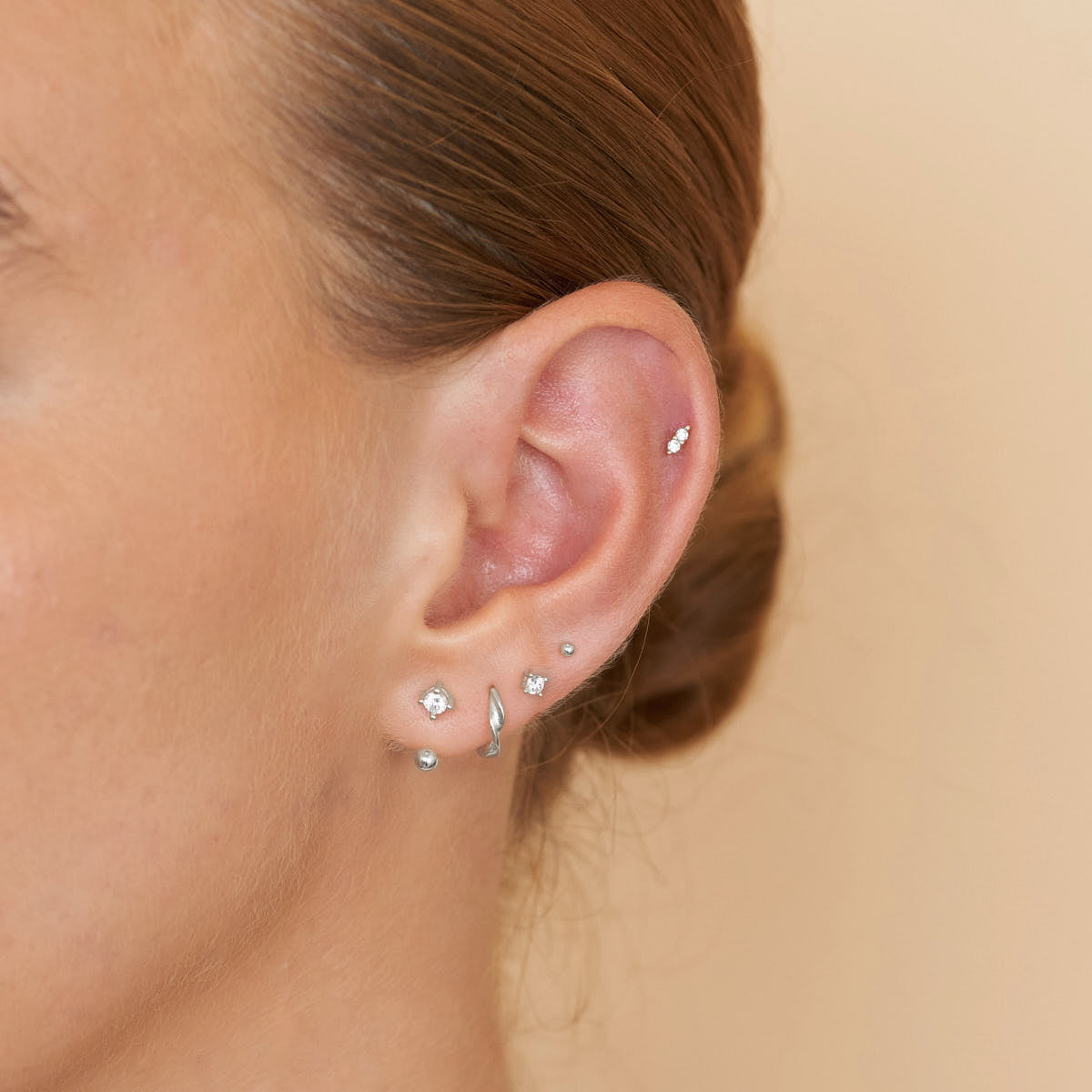 Close-up of an ear with multiple silver earrings on a beige background