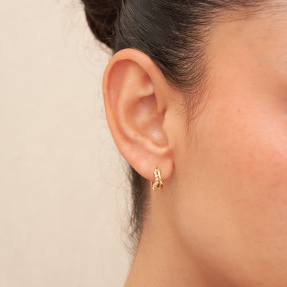Gold hoop earring worn by a person with a neutral background