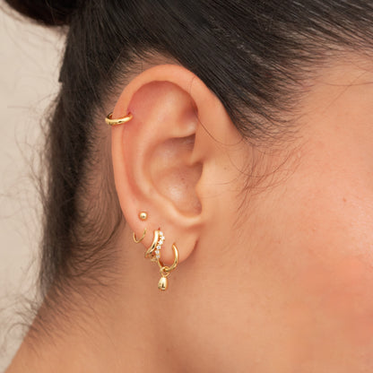 Close-up of an ear wearing gold hoop earrings with a neutral background