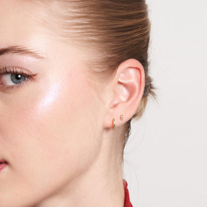 Close-up of a person wearing gold hoop earrings with a neutral background
