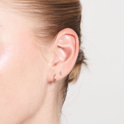 Close-up of a person's ear wearing two small hoop earrings against a neutral background