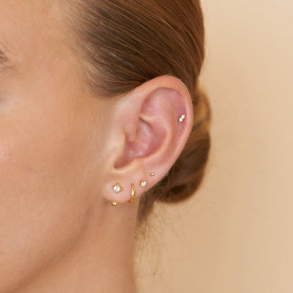 Close-up of an ear with multiple gold earrings on a beige background