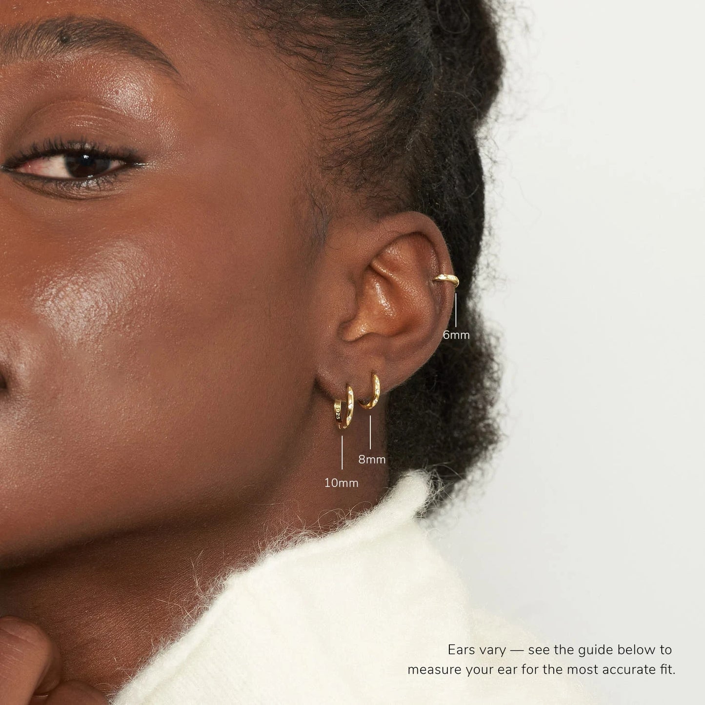 Close-up of a person wearing gold hoop earrings with size measurements on a plain background