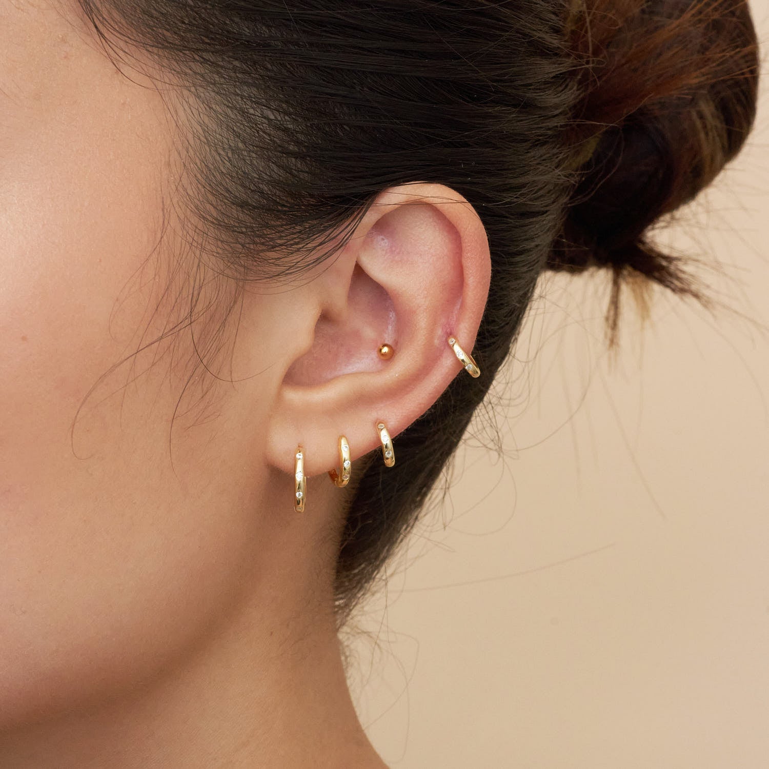 Close-up of an ear wearing gold hoop earrings with a neutral background