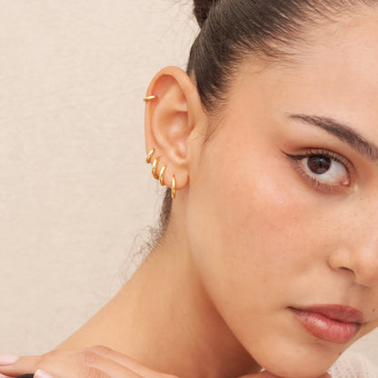 Close-up of a woman's ear with gold earrings against a neutral background