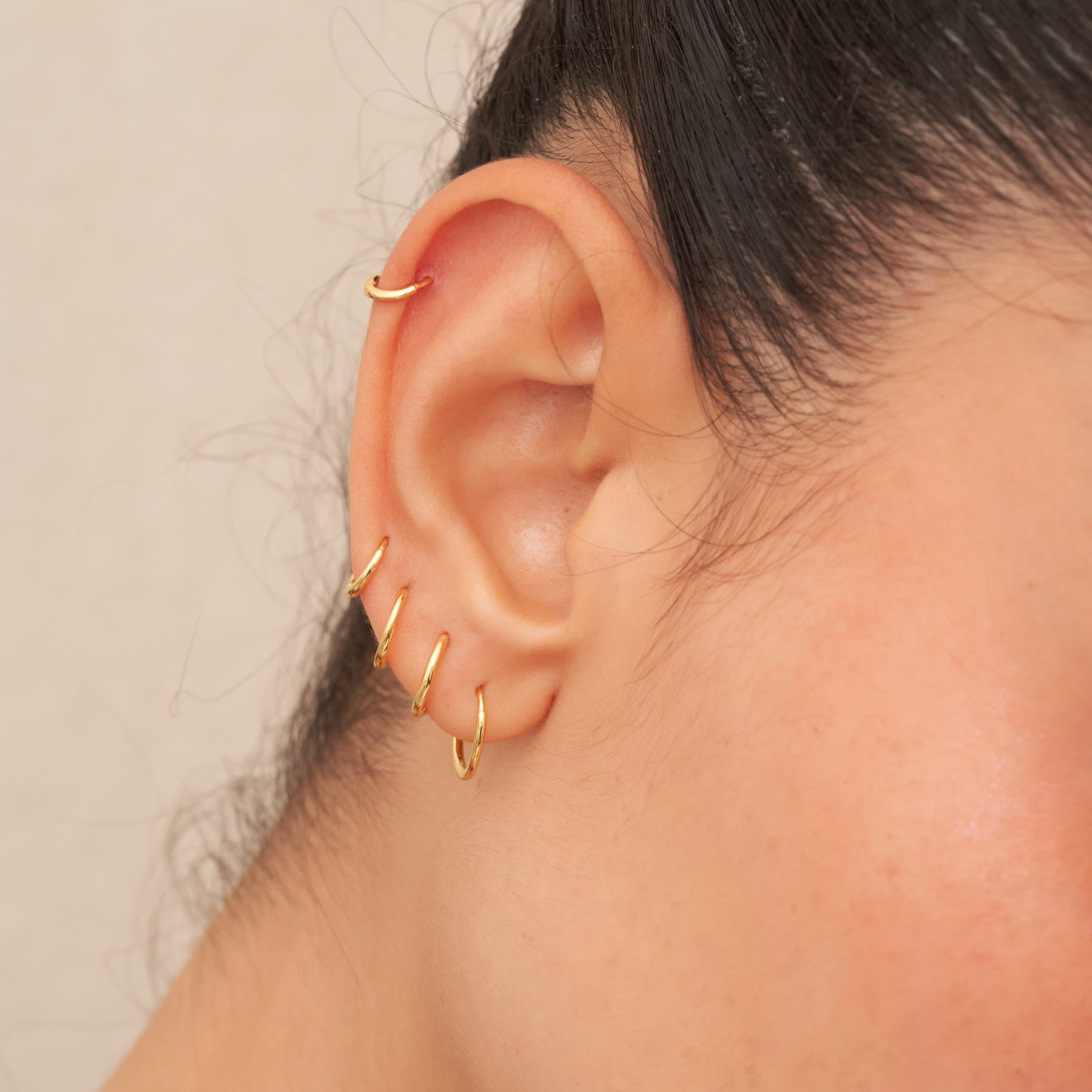 Close-up of an ear wearing gold hoop earrings with a neutral background