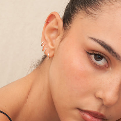 Close-up of a woman's ear with silver hoop earrings against a neutral background