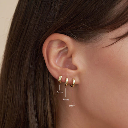 Close-up of an ear wearing gold hoop earrings with size measurements.