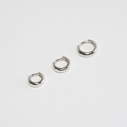 Three small silver hoop earrings on a light gray background