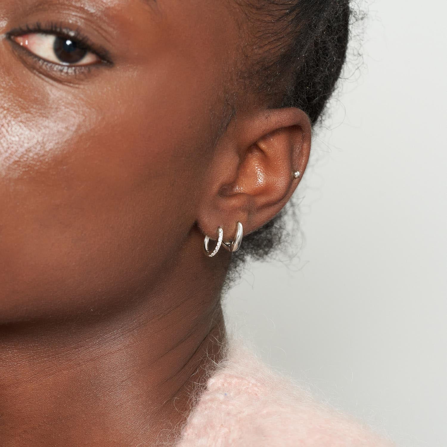 Close-up of a person wearing silver hoop earrings with a neutral background
