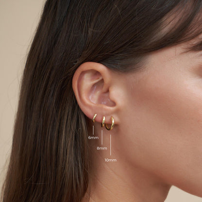 Gold hoop earrings worn by a person with an ear, showing size comparison measurements.