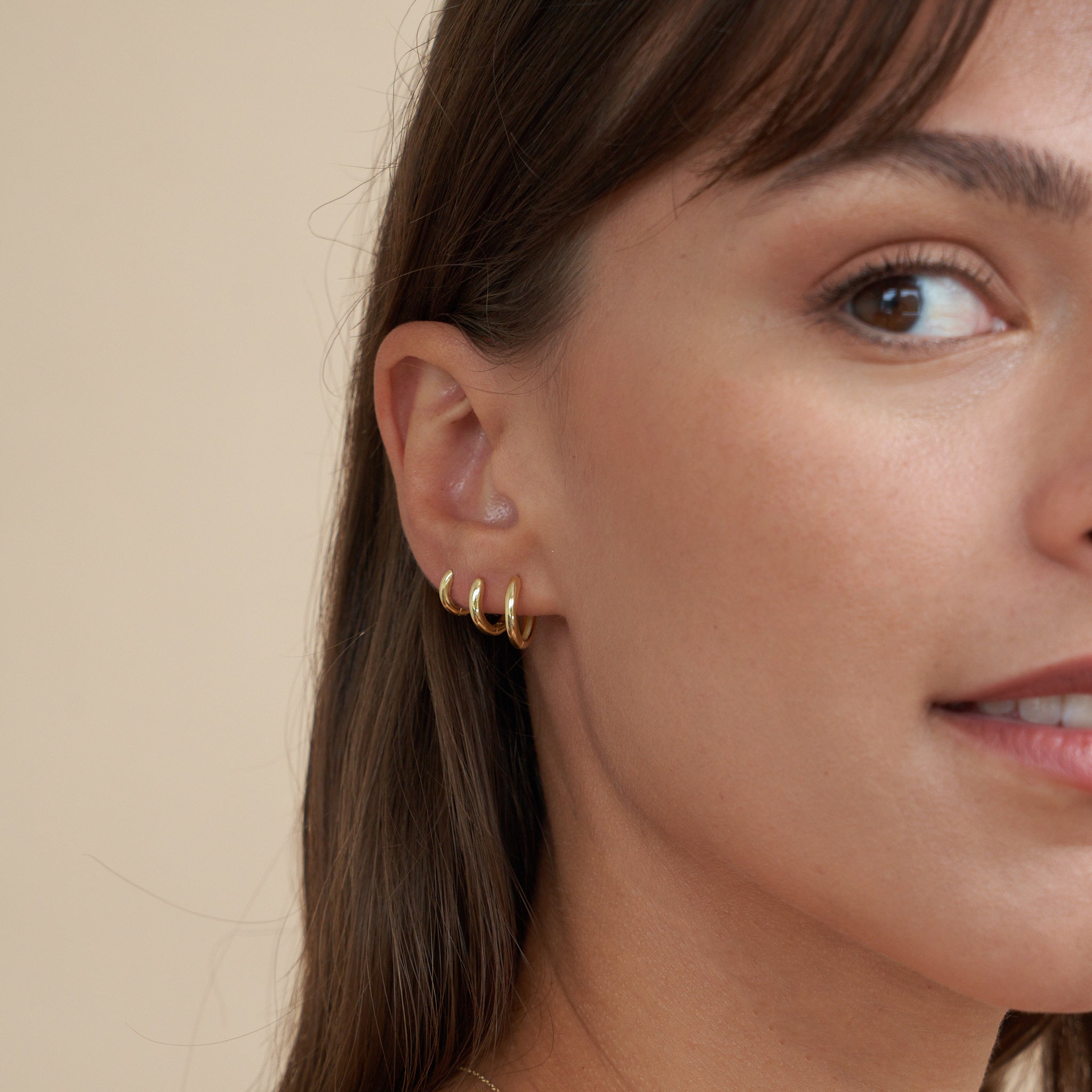Close-up of a woman wearing gold hoop earrings against a beige background