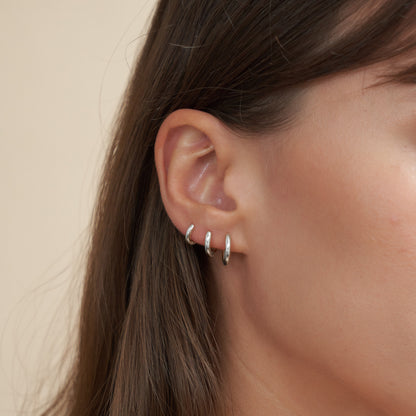 Close-up of an ear wearing silver hoop earrings with a neutral background