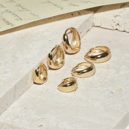 Gold hoop earrings on a textured surface with a piece of paper in the background
