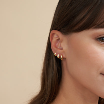 Close-up of a person wearing gold hoop earrings against a beige background
