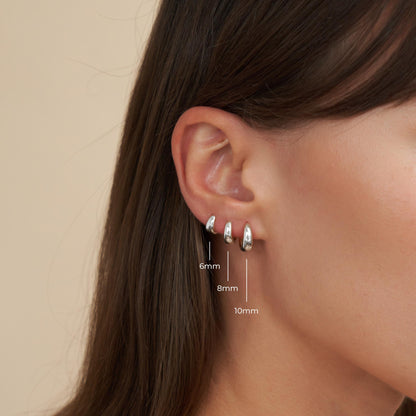 Close-up of an ear wearing silver hoop earrings with size measurements on a beige background
