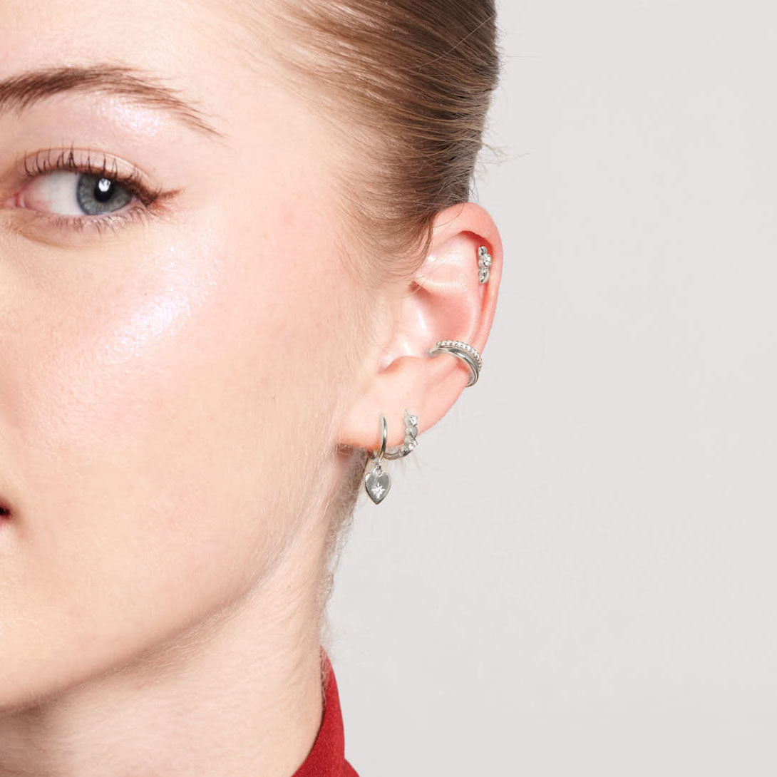 Close-up of a person's ear with multiple silver earrings on a neutral background