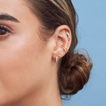 Close-up of a person's ear with gold earrings against a blue background