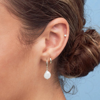 Close-up of an ear wearing a silver earring with a pearl drop against a blue background