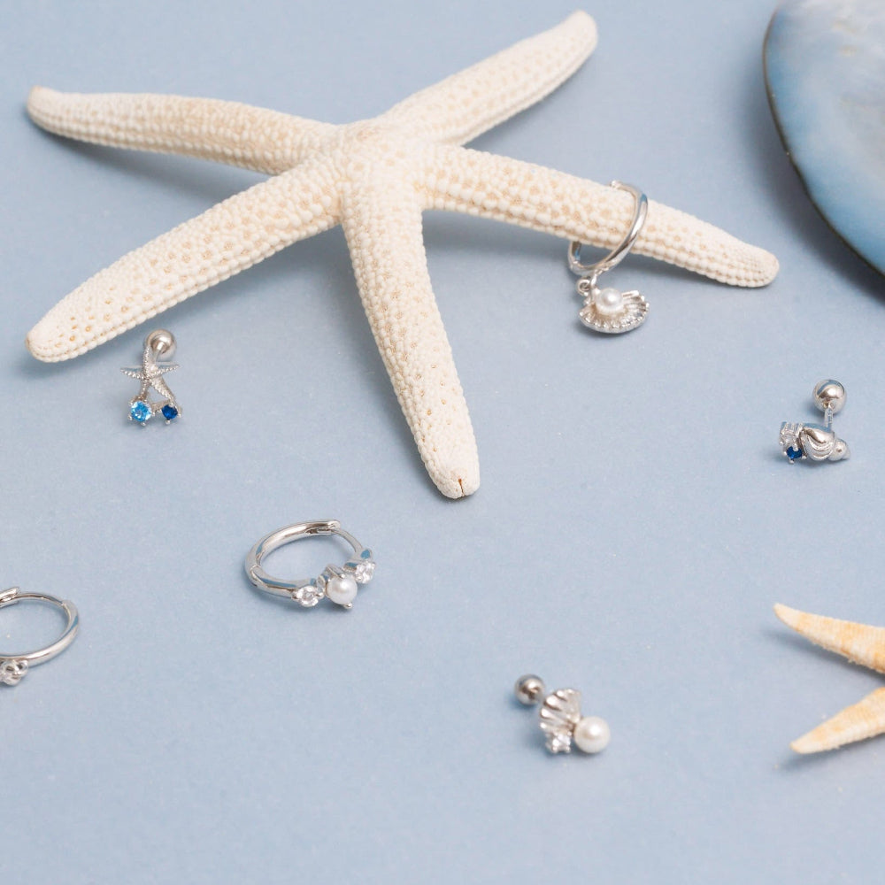 Silver jewelry including rings and earrings on a light blue background with starfish and shells.
