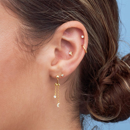 Close-up of an ear wearing gold earrings with a blue background