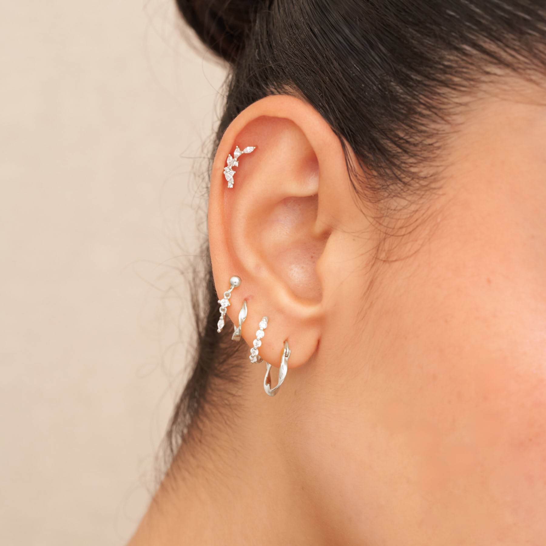 Close-up of an ear wearing silver hoop earrings with a neutral background