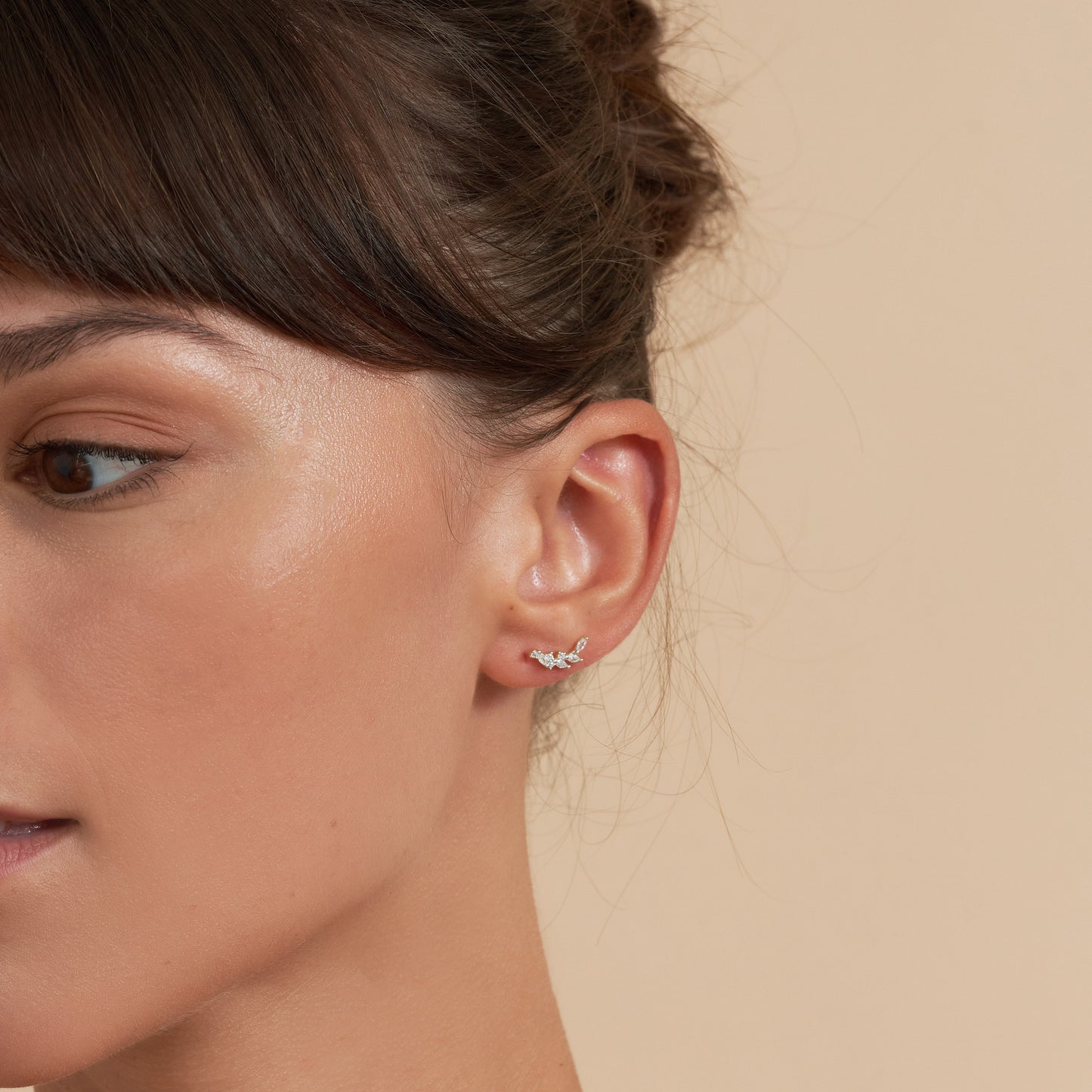 Close-up of a woman's ear wearing a small earring against a beige background