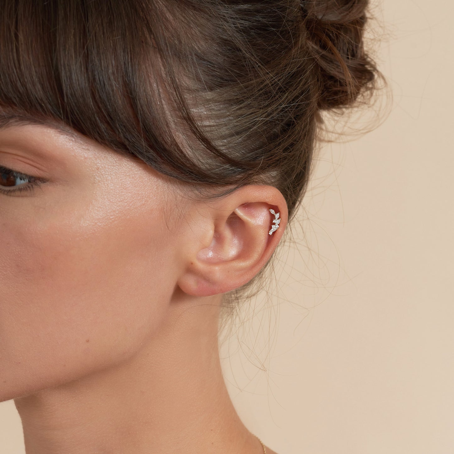 Close-up of a person's ear with an earring on a beige background