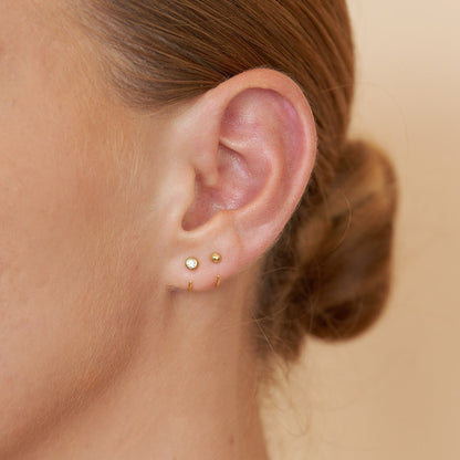 Close-up of an ear wearing gold stud earrings with a blurred background