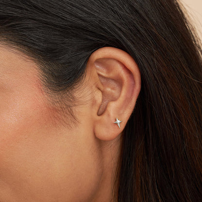 Close-up of an ear wearing a star-shaped earring with dark hair and skin.