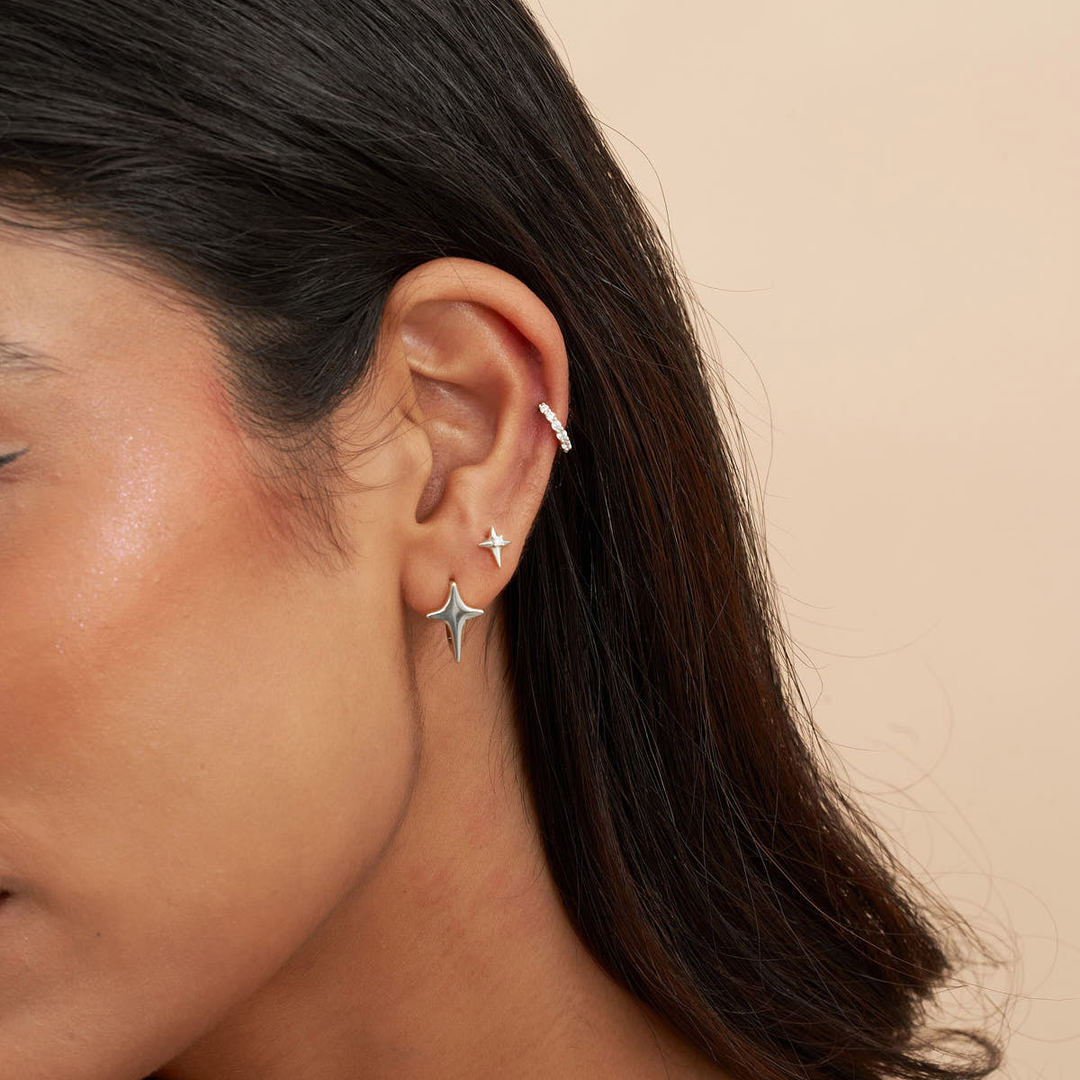Close-up of a person wearing star-shaped earrings against a beige background