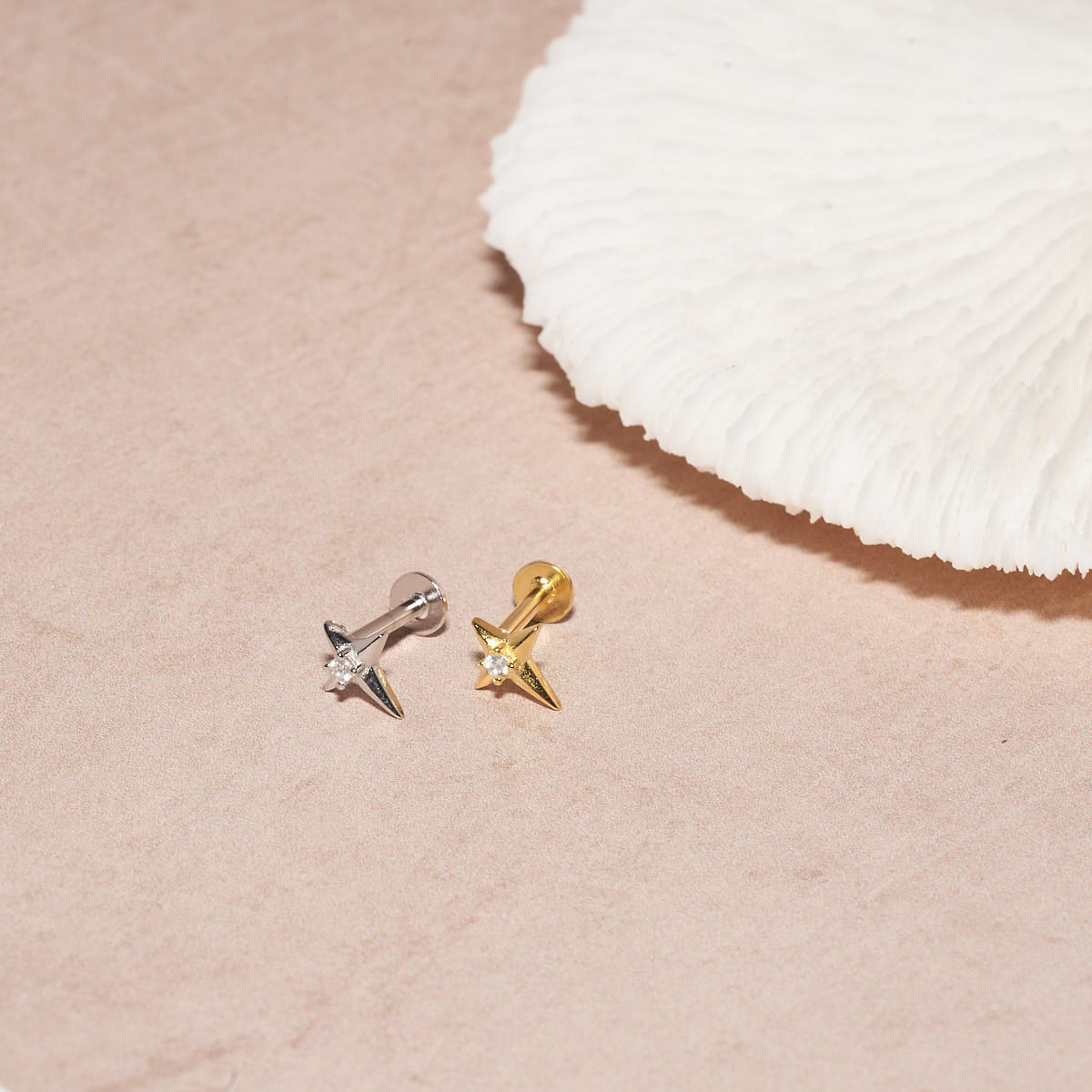 Pair of gold and silver spike earrings on a pink surface with a white shell.