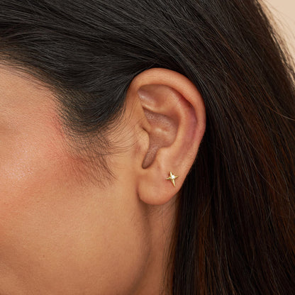 A close-up image of a person's ear wearing a gold labret stud with a star design.