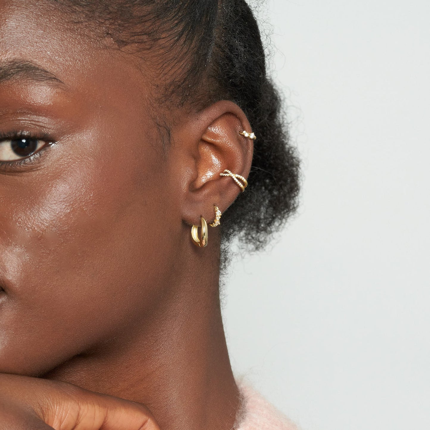 Close-up of a person's ear with gold earrings against a neutral background