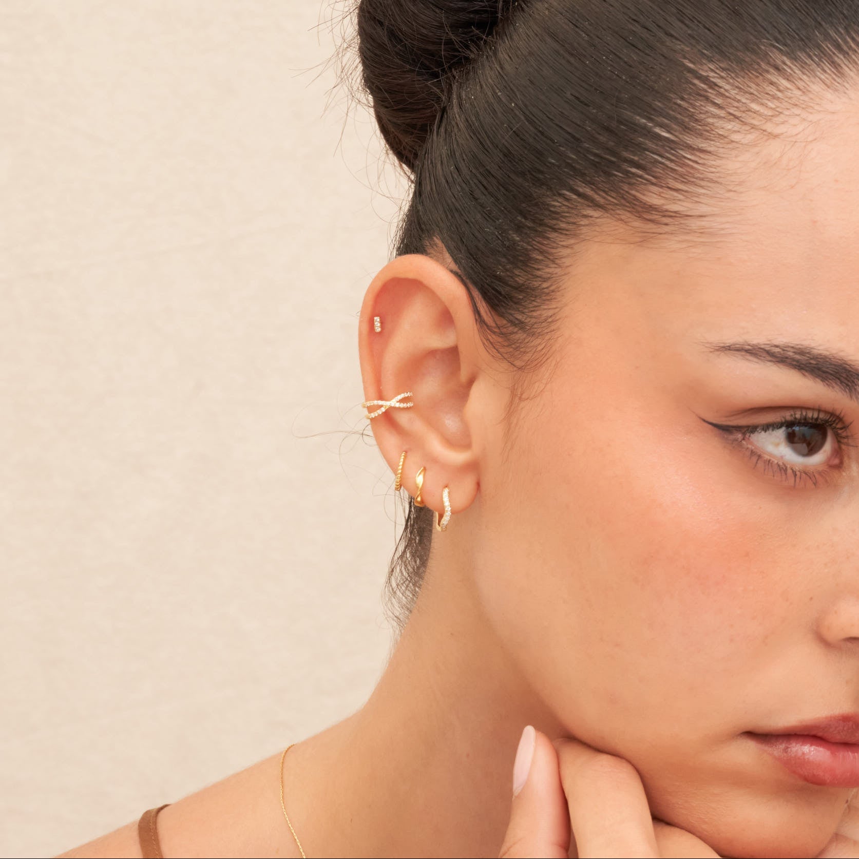 Close-up of a woman wearing gold hoop earrings with a neutral background