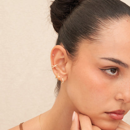 Close-up of a woman wearing gold hoop earrings with a neutral background