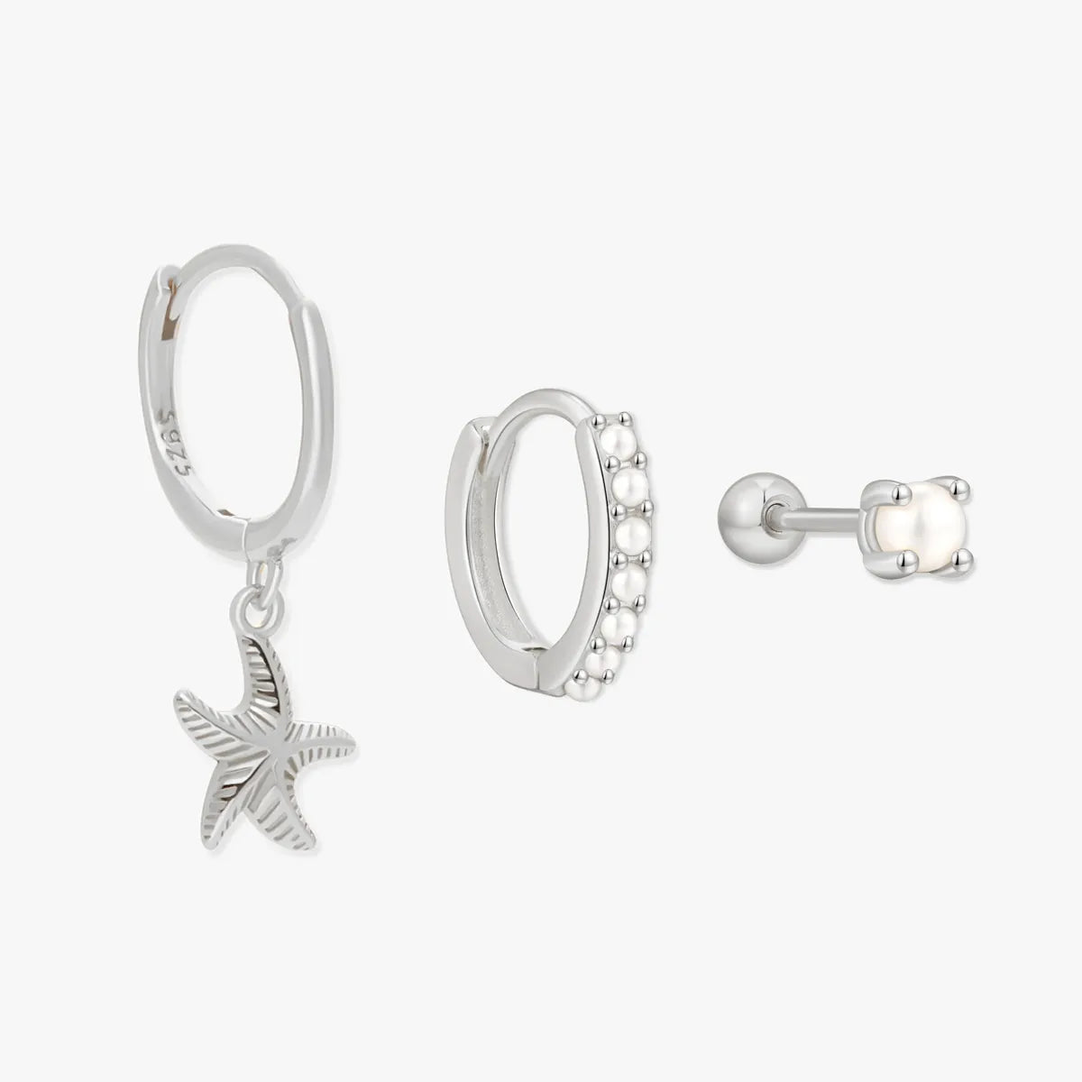 Set of silver earrings including a starfish charm, hoop earrings with embedded stones, and a stud earring on a white background.