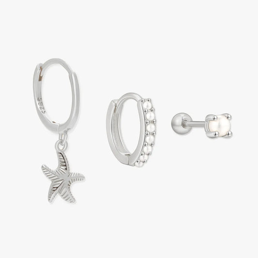 Set of silver earrings including a starfish charm, hoop earrings with embedded stones, and a stud earring on a white background.