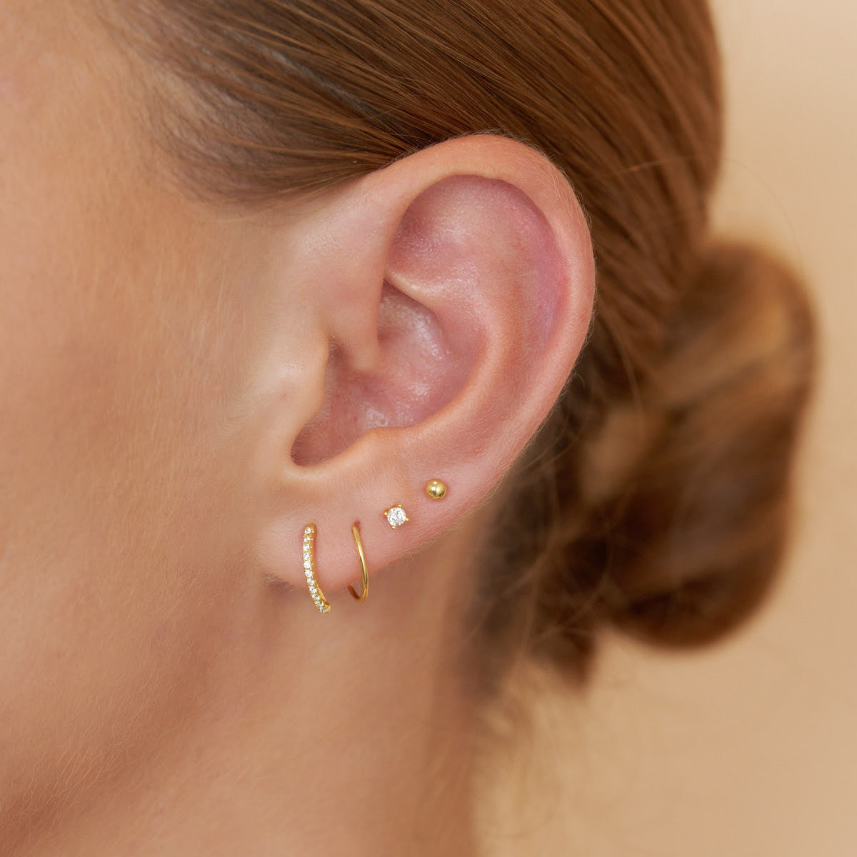 Close-up of an ear wearing gold hoop earrings with small gemstones.