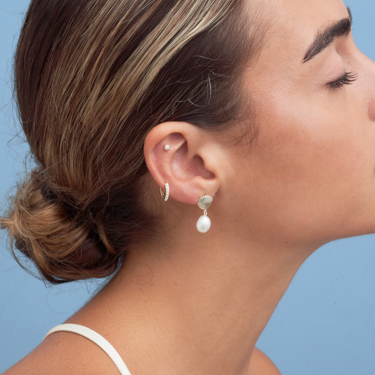 Close-up of a woman wearing pearl earrings against a blue background