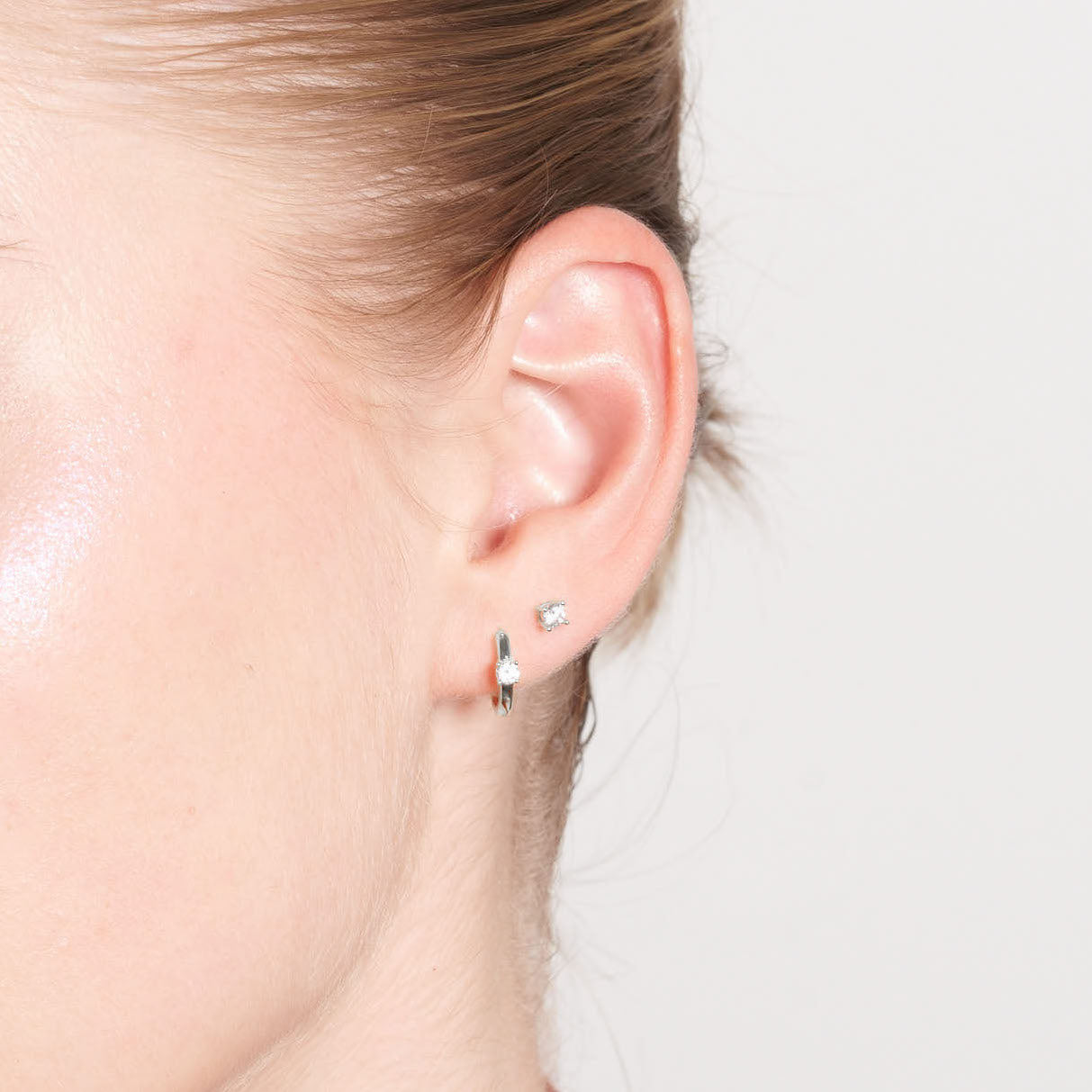 Close-up of an ear wearing a small earring on a neutral background