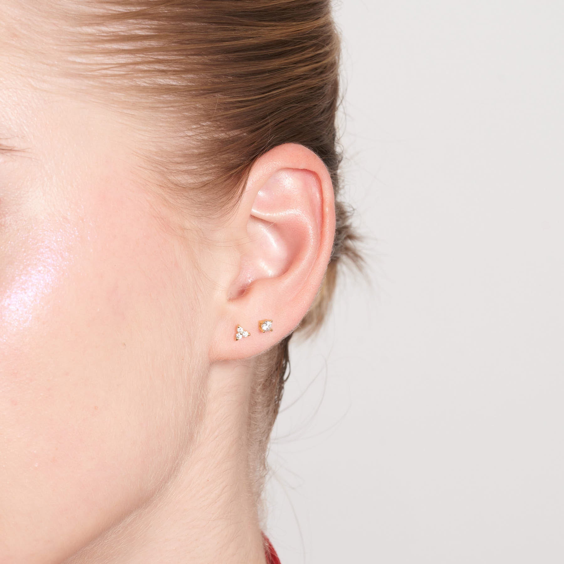 Close-up of an ear wearing two small earrings on a neutral background