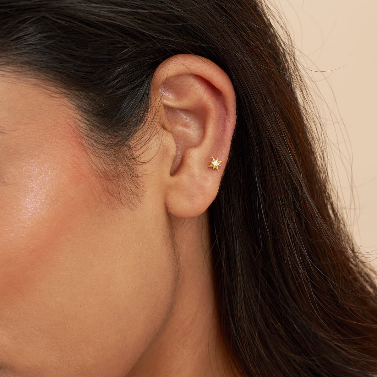 Close-up of an ear wearing a gold star-shaped earring with a neutral background