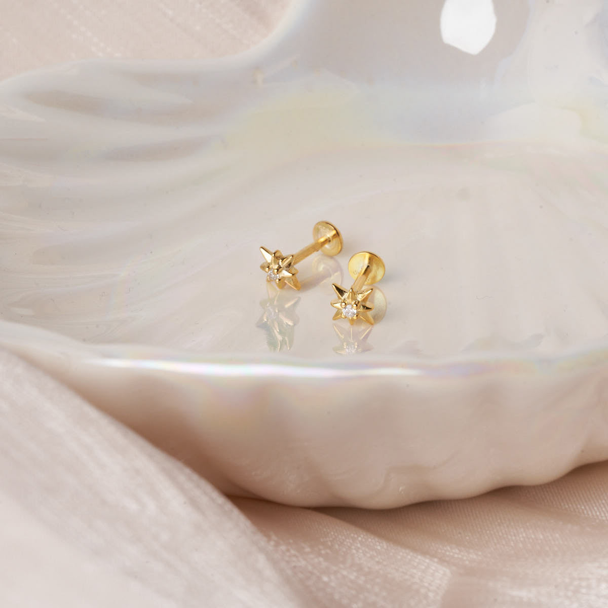 Gold stud earrings on a white dish with a soft pink fabric background