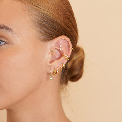 Close-up of a person's ear with multiple gold earrings on a beige background