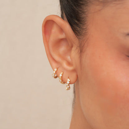 Close-up of an ear wearing gold hoop earrings with a neutral background