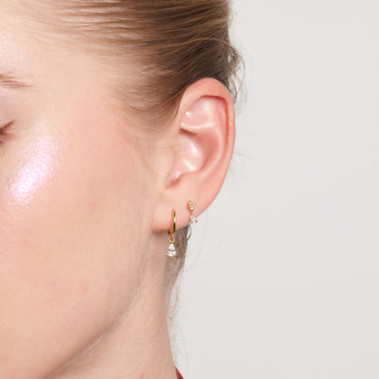 Close-up of a person wearing gold hoop earrings with a plain background