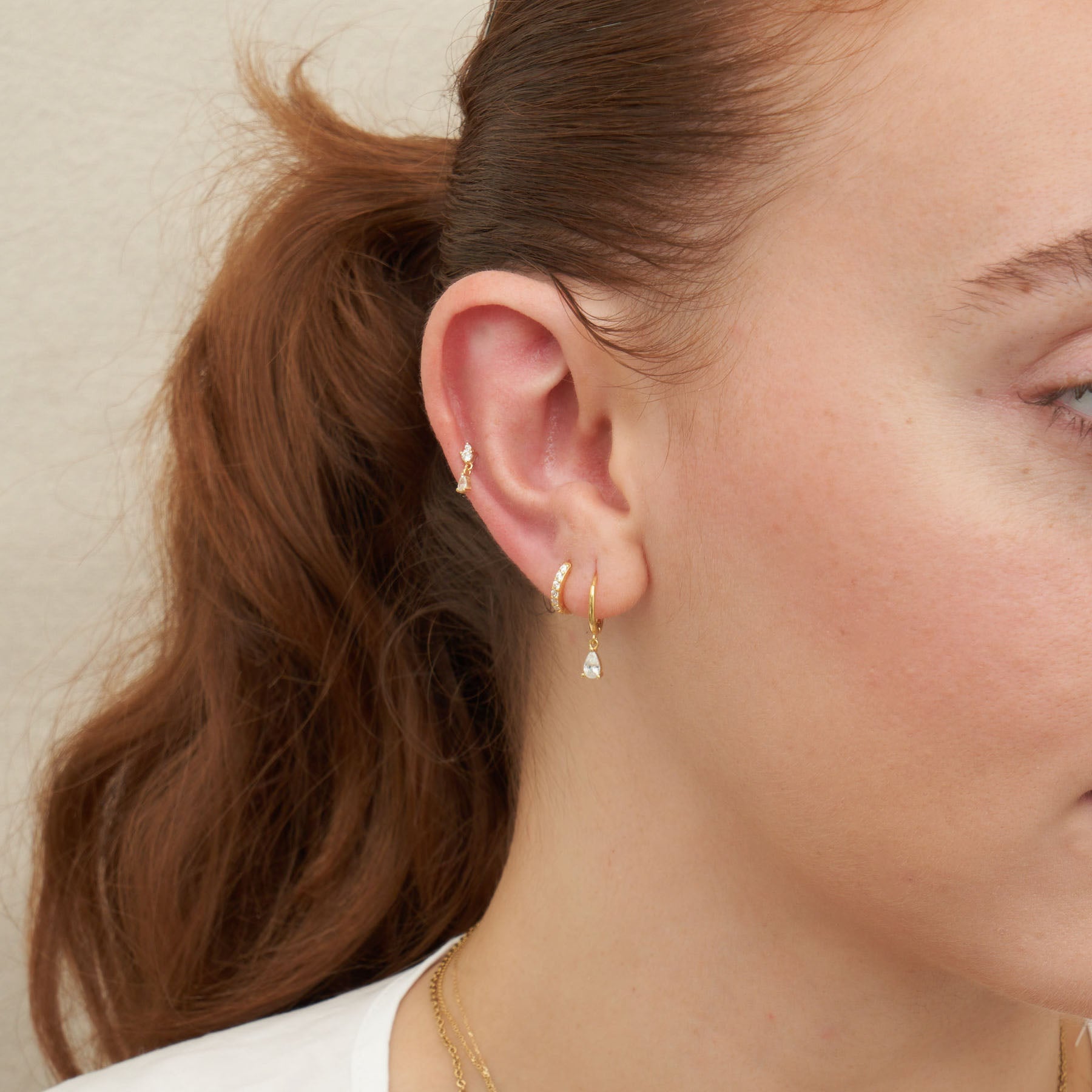 Close-up of a person wearing gold earrings with a neutral background